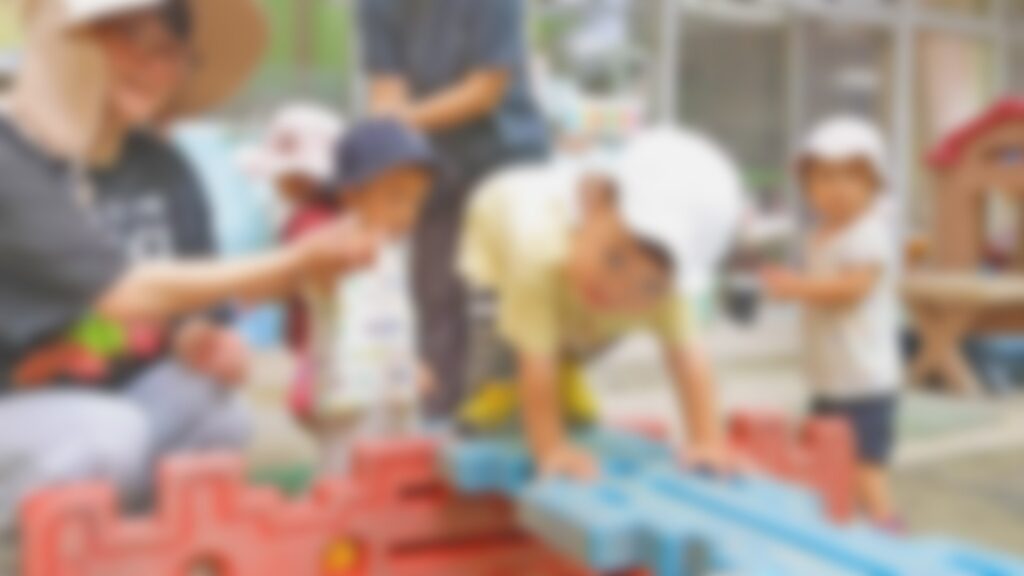 ブロックをつないだ道を手をついて進む子どもたちと、手を取って支える先生